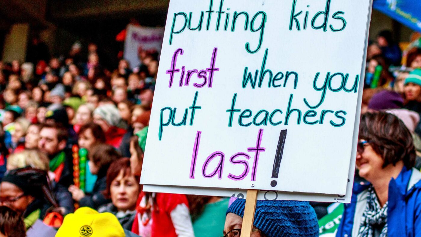 A sign amongst the crowd at a strike action. Sign reads: You aren't putting kids first when you put teachers last!